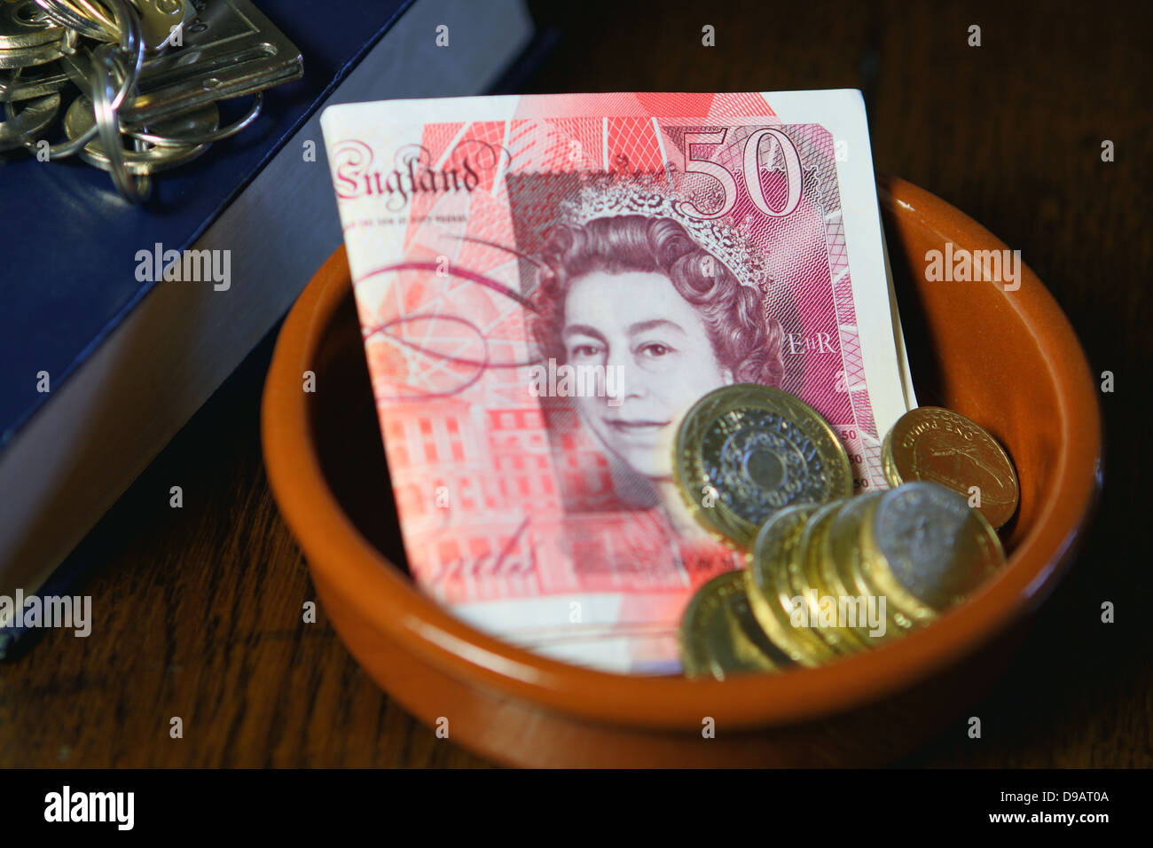 Eine braune Schale mit Sterling £50-Banknoten und-Münzen neben Teil eines Buches mit Tasten an der Spitze Stockfoto