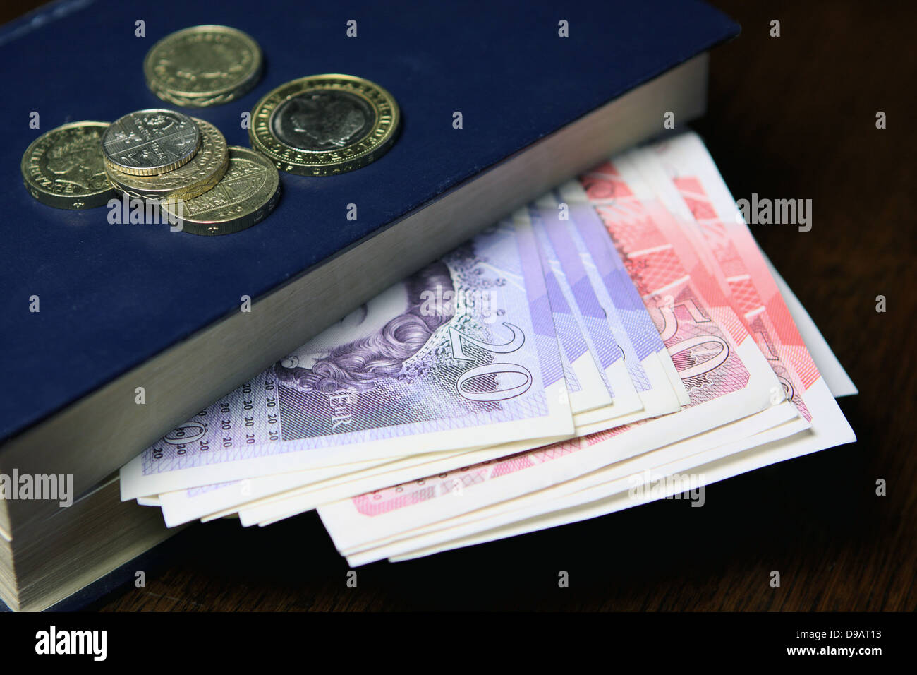 Münzen auf ein Buch mit Sterling £50 und £20 Noten Stockfoto