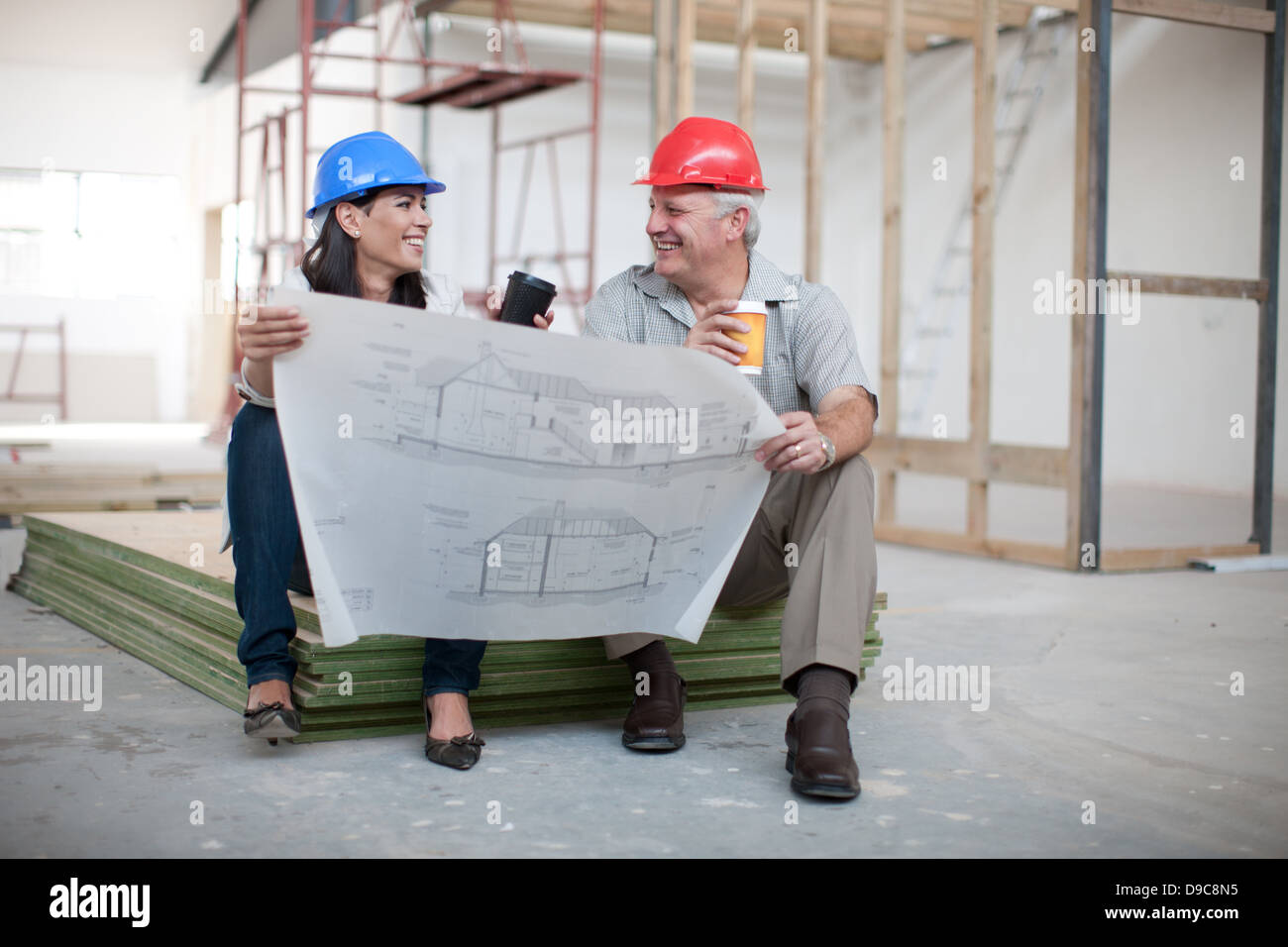 Männliche und weibliche Bauarbeiter sitzen hält Kaffee und eine Blaupause Stockfoto