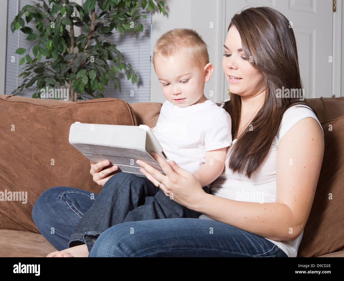 Hübsche junge kaukasischen Mutter und Sohn blondes Kleinkind sitzt zu Hause auf Sofa zusammen auf einem drahtlosen mobilen Tablet lesen. Stockfoto