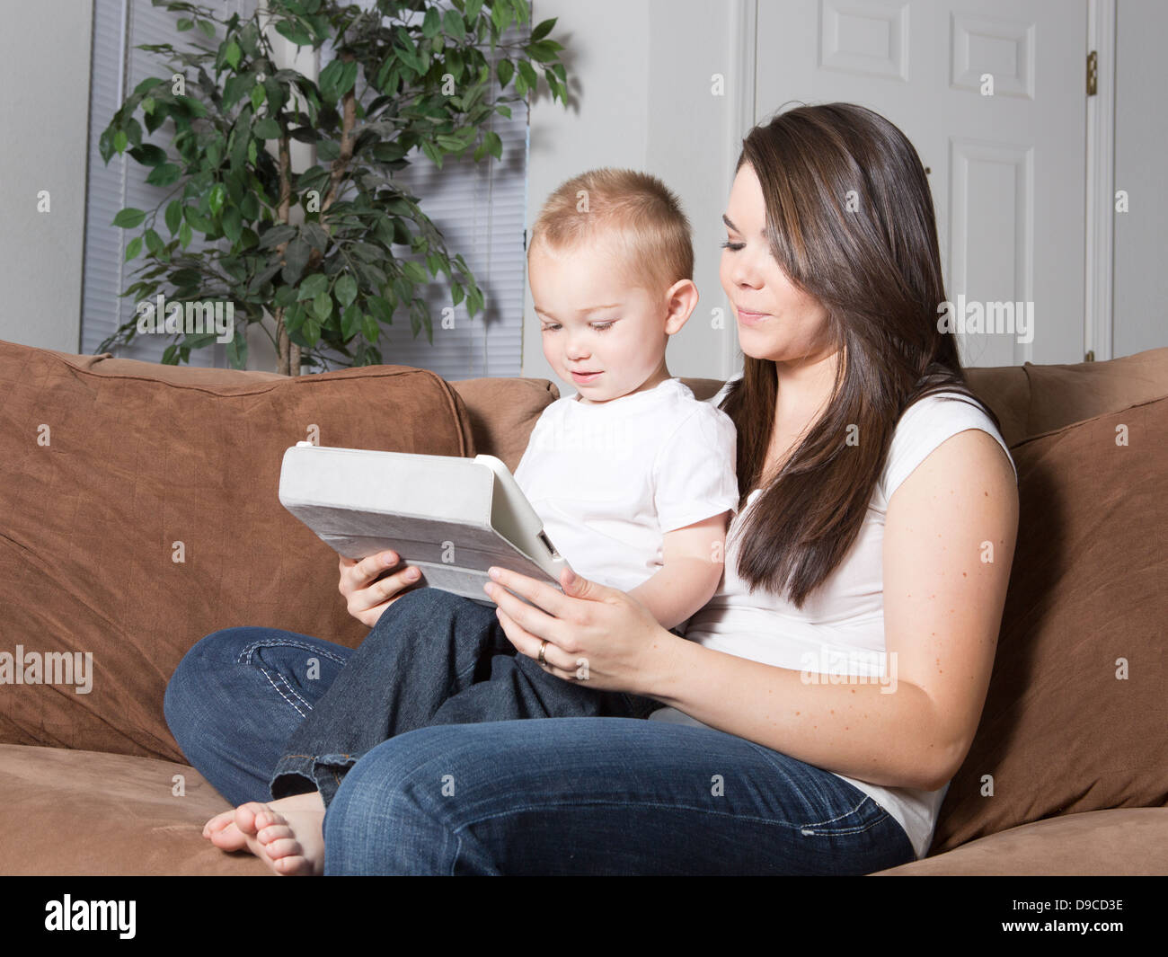 Hübsche junge kaukasischen Mutter und Sohn blondes Kleinkind sitzt zu Hause auf Sofa zusammen auf einem drahtlosen mobilen Tablet lesen. Stockfoto