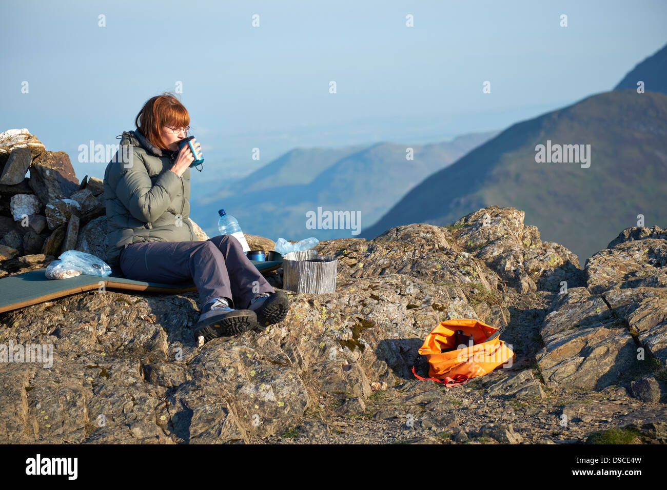 Eine weibliche Wanderer genießen eine frühen Morgen Tasse Tee nach camping auf dem Gipfel des Robinson im Lake District Stockfoto