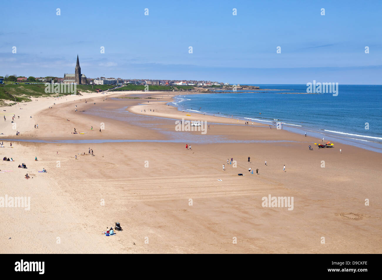 Sandstrand in Tynemouth mit Sonnenanbeter und Schwimmer mit Kirchturm in der Ferne Stockfoto