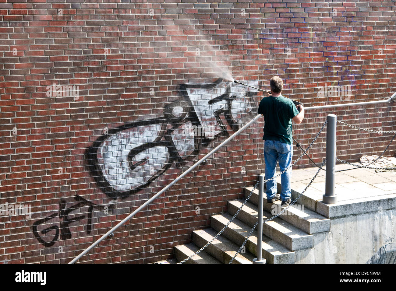 Man entfernt Graffiti von einer Mauer, einer entfernt Graffiti an einem Fluss, Stockfoto