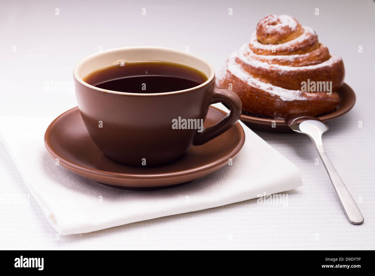 Tasse schwarzer Tee auf weiße Serviette mit süße Brötchen und Teelöffel Stockfoto