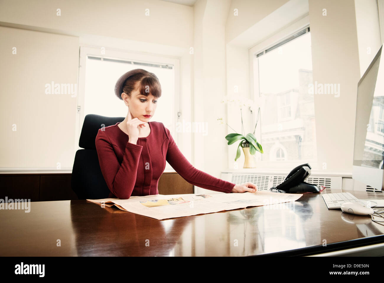 Frau sitzt am Schreibtisch lesen Zeitung Stockfoto