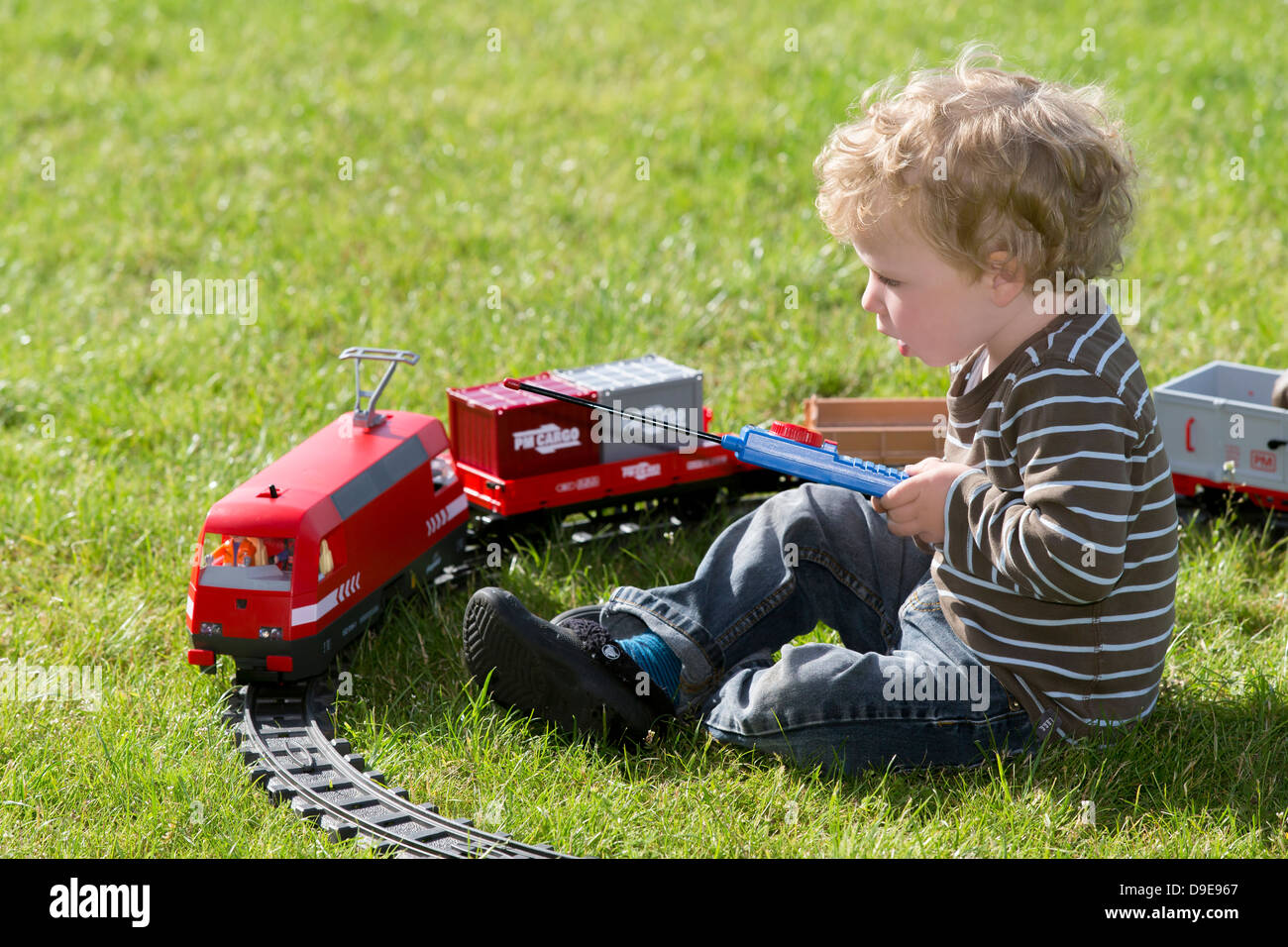 Infant Boy, 2 Jahre, mit elektrischen Spielzeugeisenbahn im Garten spielen Stockfoto