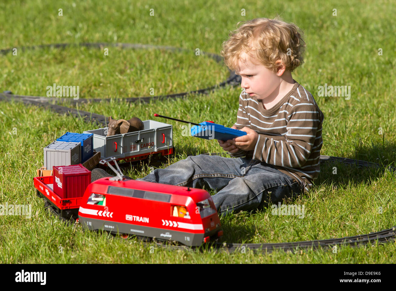 Infant Boy, 2 Jahre, mit elektrischen Spielzeugeisenbahn im Garten spielen Stockfoto