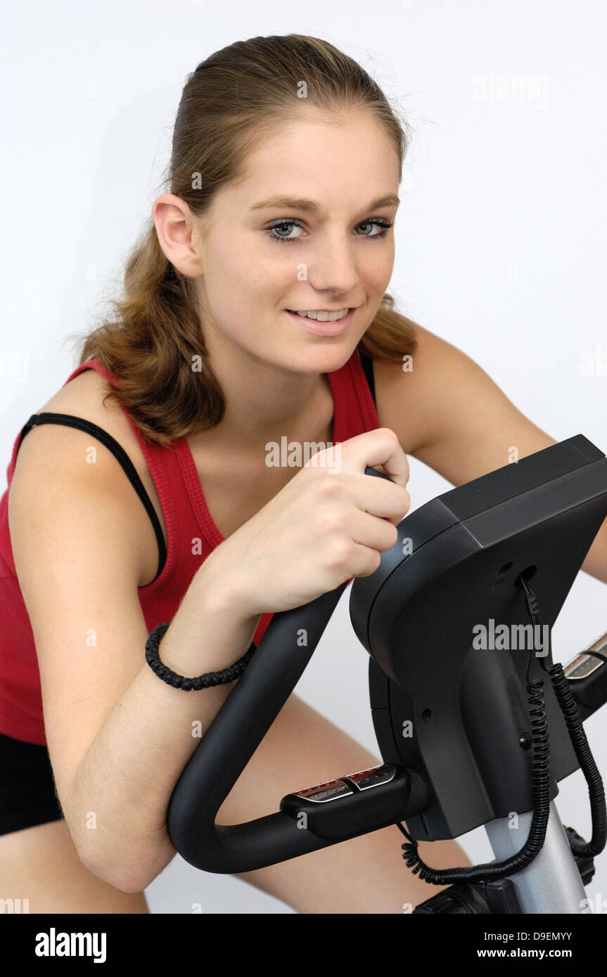 (Model Release) Junge Frau im roten Sport Hemd sitzt auf einem Fahrradergometer Stockfoto