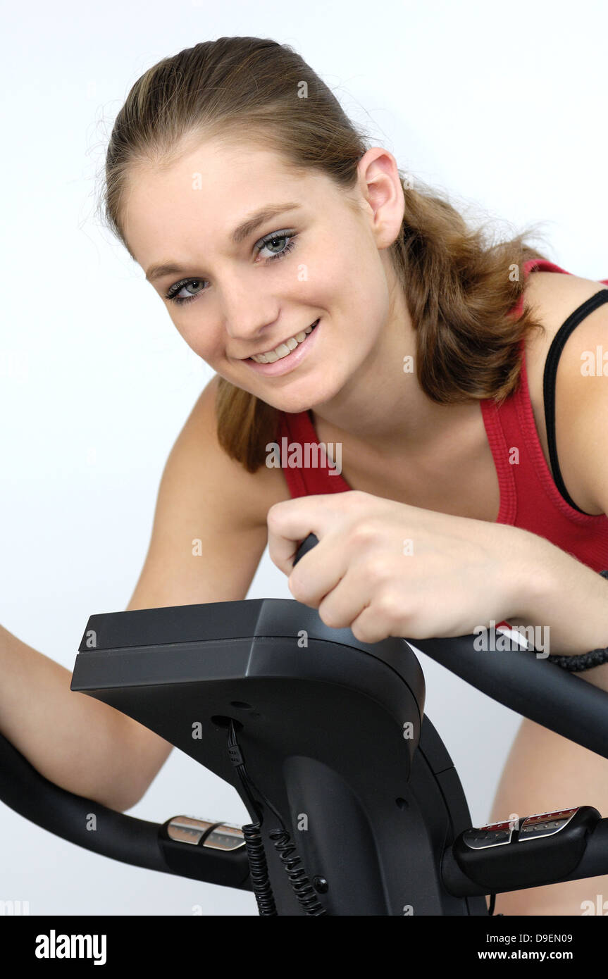 (Model Release) Junge Frau im roten Sport Hemd sitzt auf einem Fahrradergometer Stockfoto