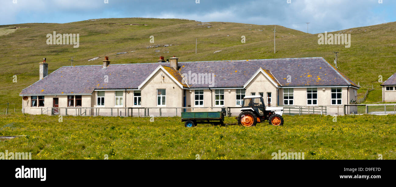 Ein Traktor geht vor einer ländlichen Schule auf der Insel Barra in den äußeren Hebriden. Stockfoto