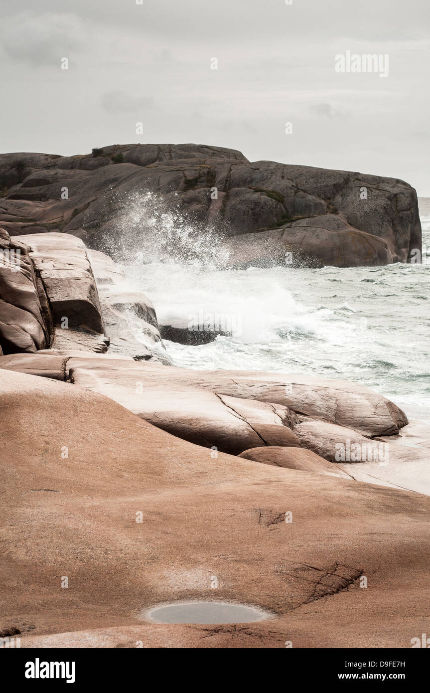 Wellen plätschern gegen roten Granitfelsen Stockfoto