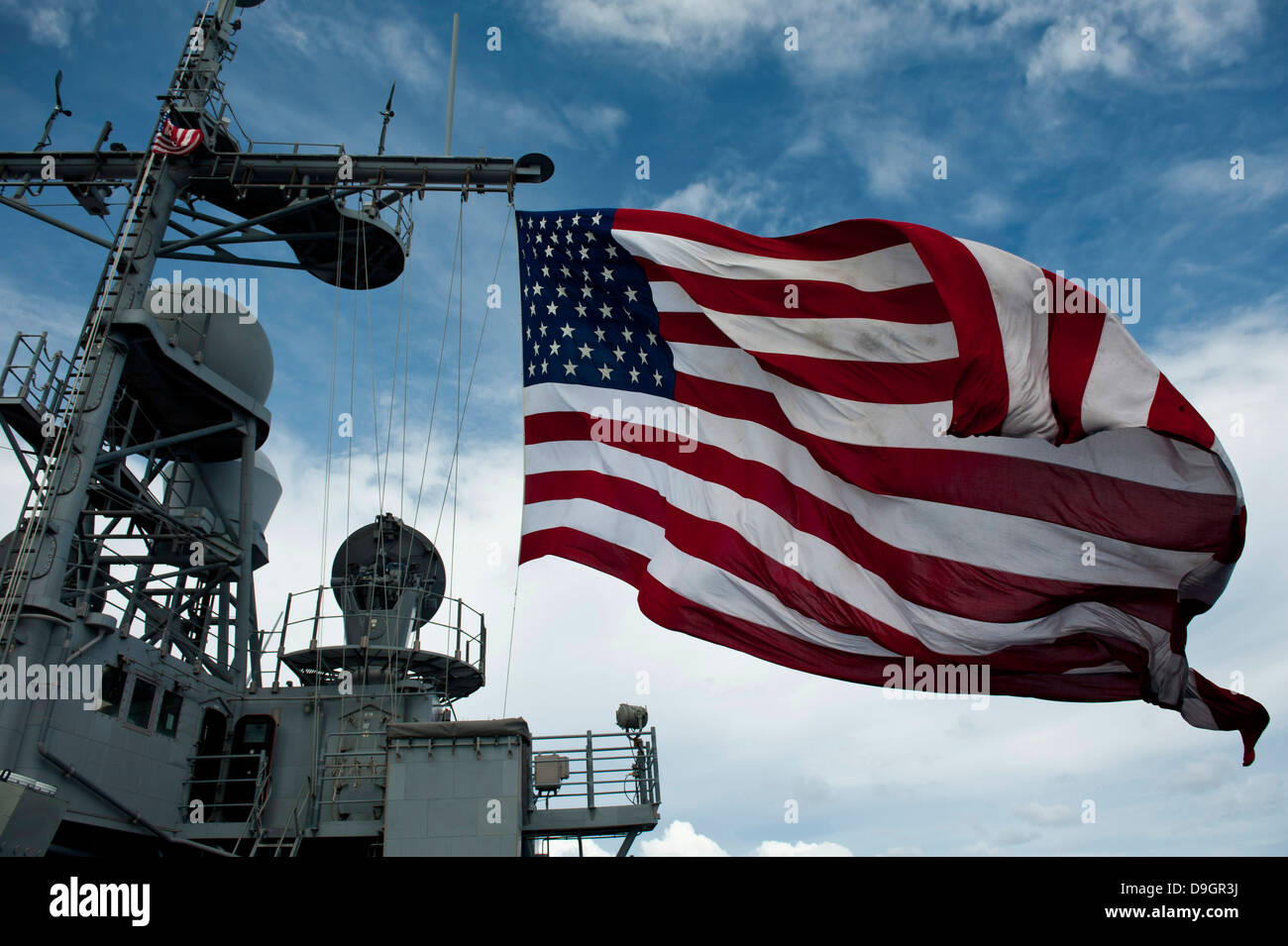 USS Cowpens fliegt eine große amerikanische Flagge während ein scharfer Munition Waffen zu schießen. Stockfoto