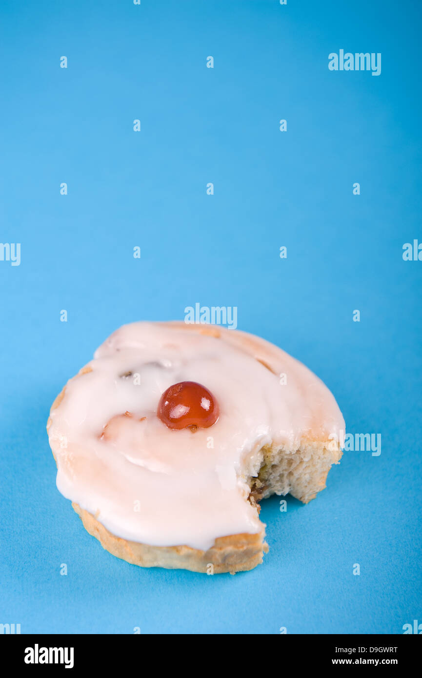 Geeiste Kuchen mit einer Kirsche auf der Oberseite und einen großen Happen, vor einem blauen Hintergrund. Stockfoto