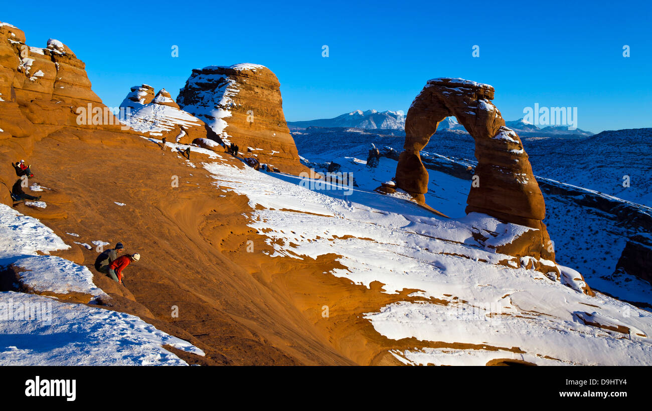 Gruppen von Menschen betrachten Delicate Arch mit Schnee im Winter bei Sonnenuntergang, Arches-Nationalpark, Utah, Vereinigte Staaten von Amerika Stockfoto
