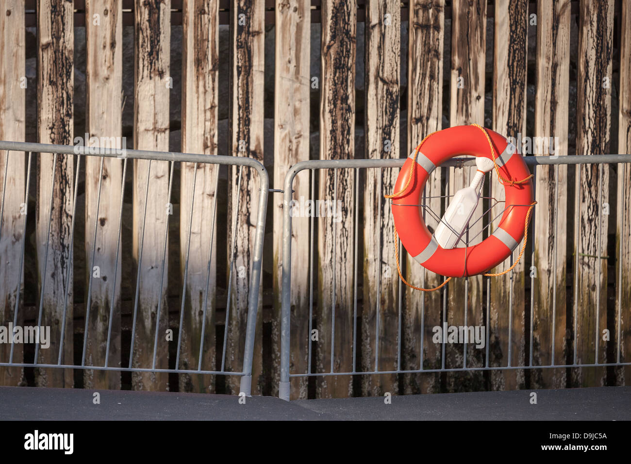Roten Rettungsring mit Seil an Metallgeländer über verwitterten Holzwand im Hafen Stockfoto