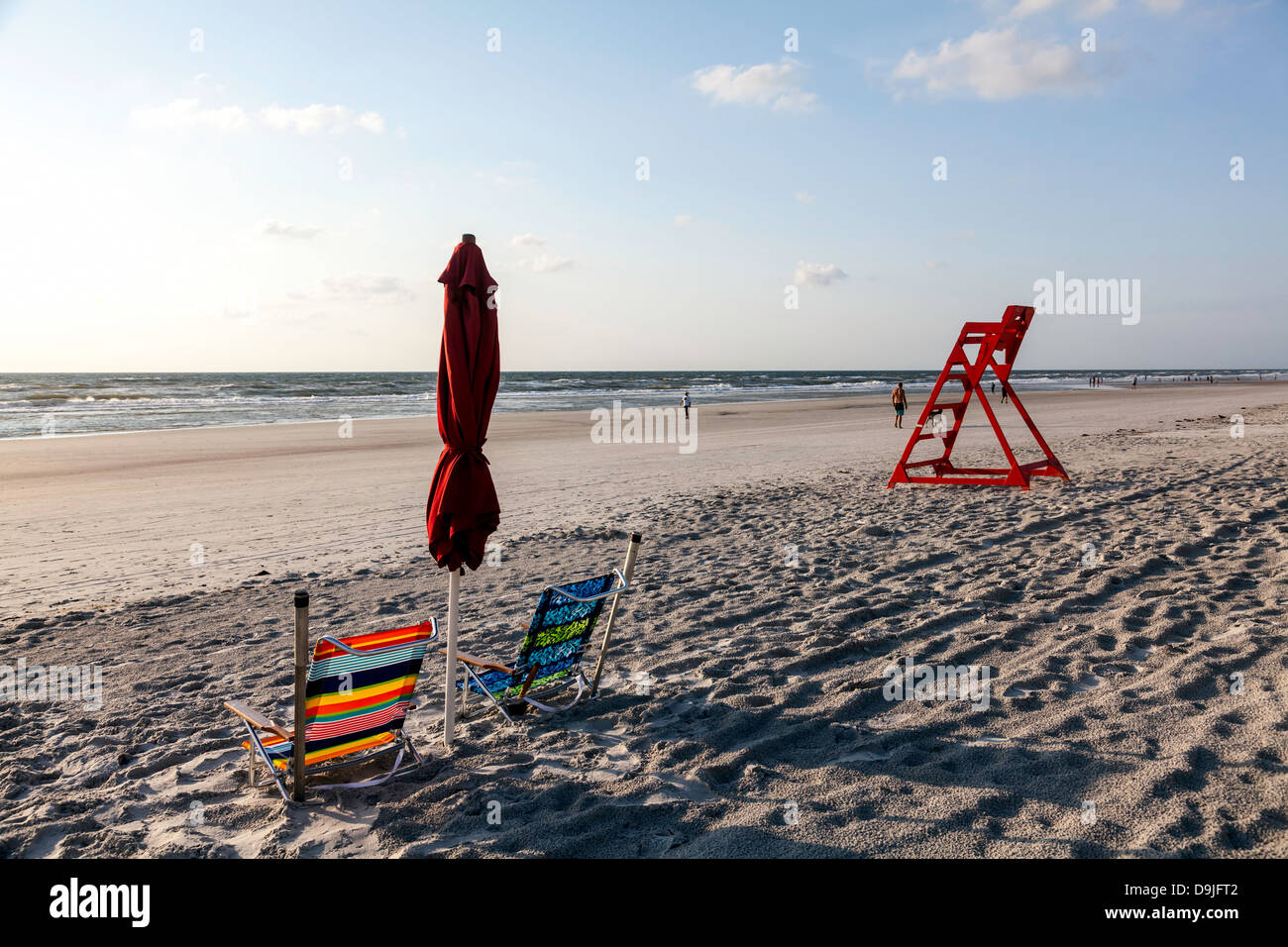 Bunt gestreifte Strand Klappstühle und gefalteten roten Regenschirm mit orange Leben bewachen Stühle und Atlantischen Ozean hinaus sichtbar. Stockfoto