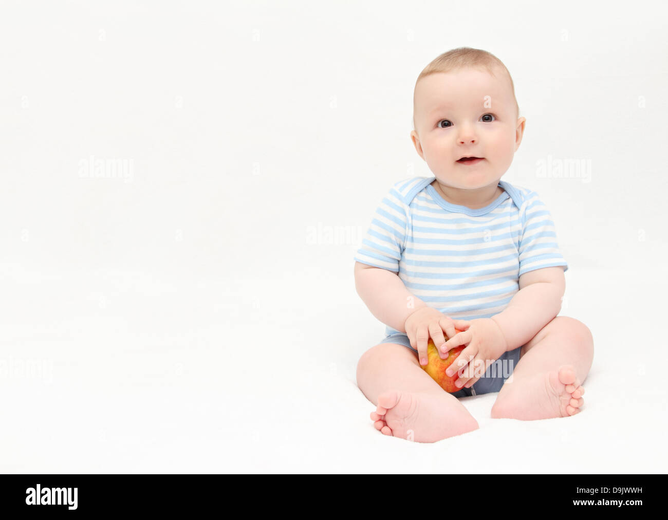 schönes glückliches Baby Junge sitzt auf weißen Bett mit Apfel Stockfoto