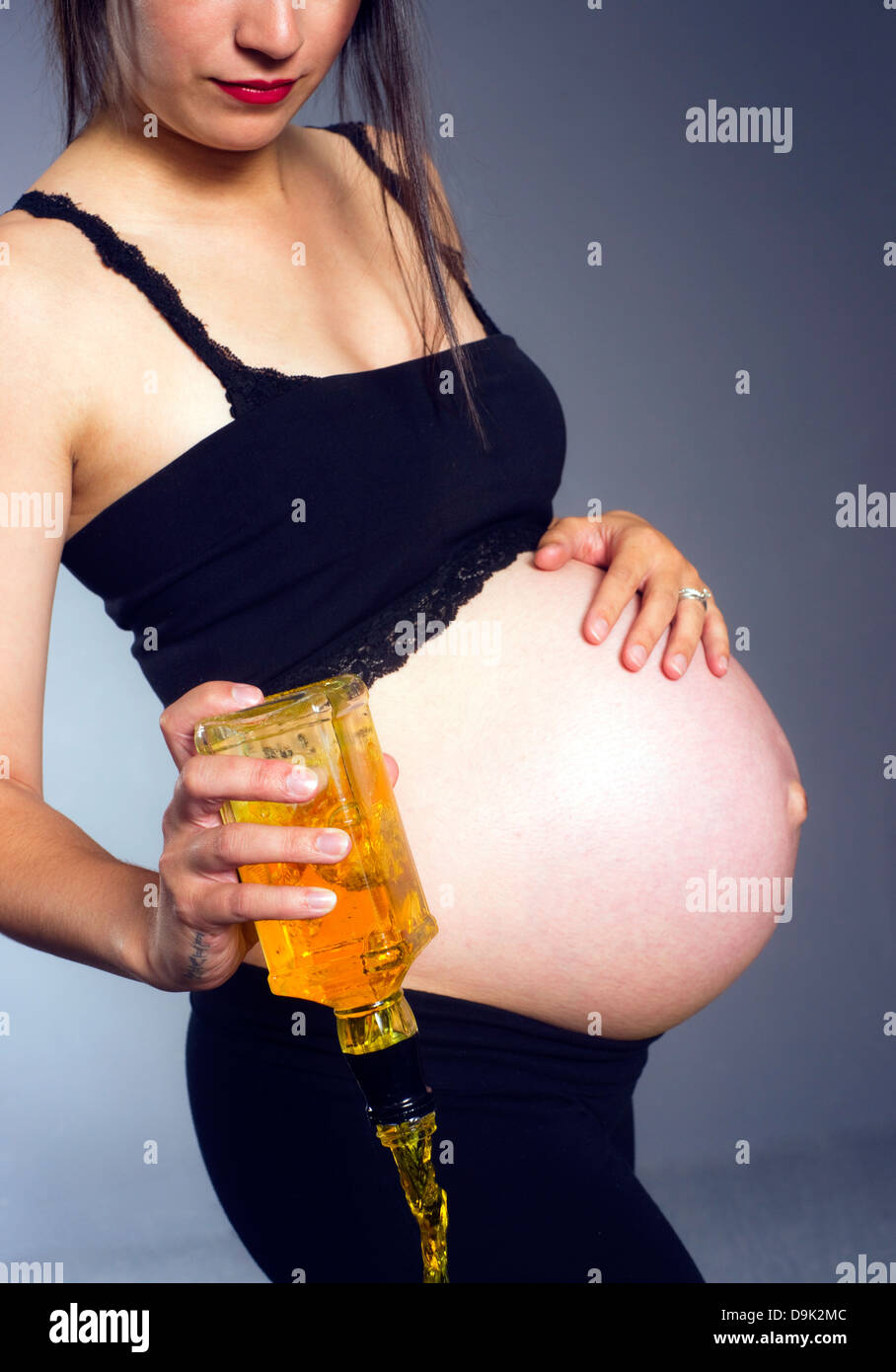 Vertikale Zusammensetzung der Frau gießt eine Flasche Whisky hart während der Schwangerschaft Stockfoto