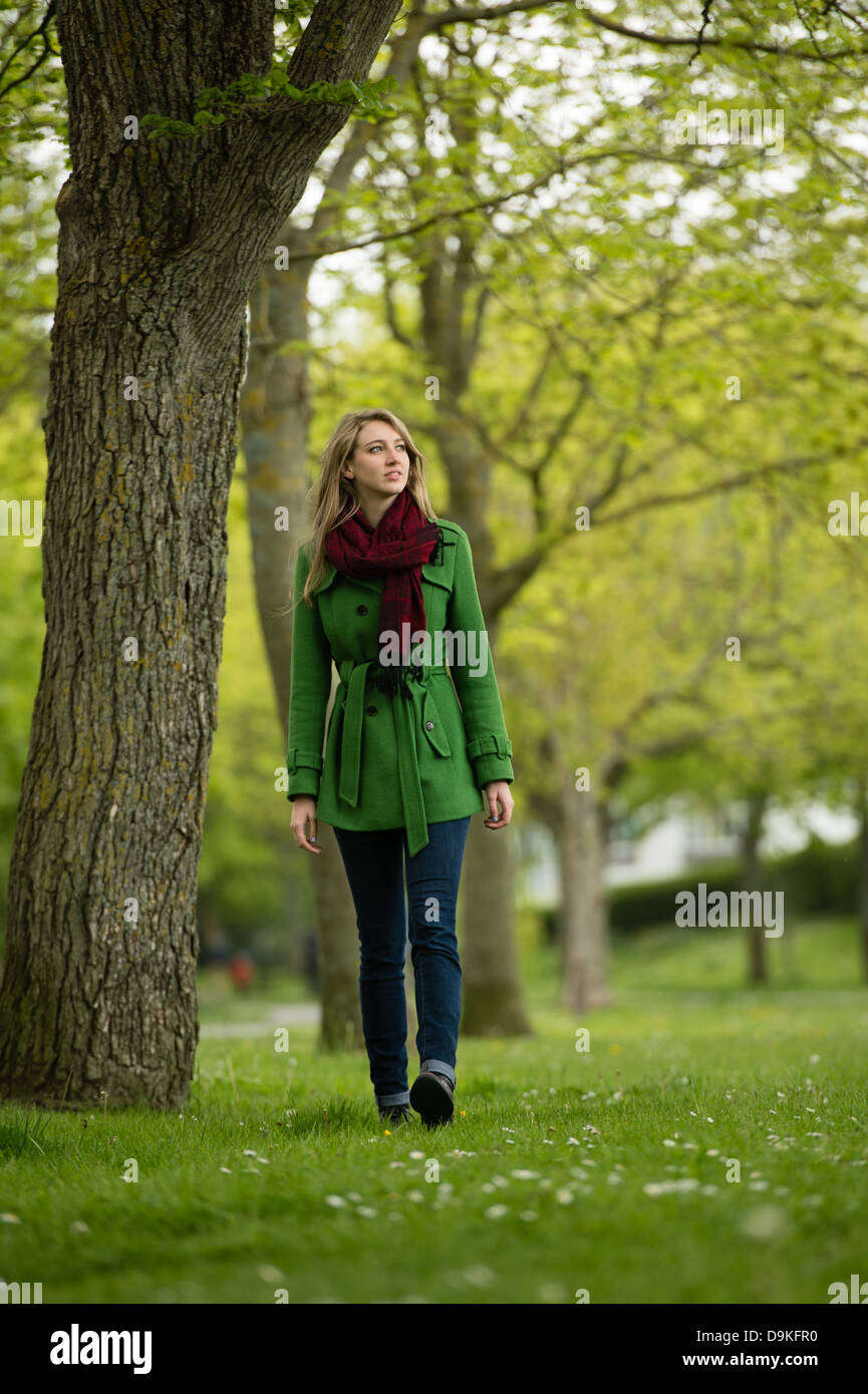 Eine junge Frau trägt einen grünen Mantel alleine im Wald Waldpark spazieren an einem Frühlingstag, UK Stockfoto