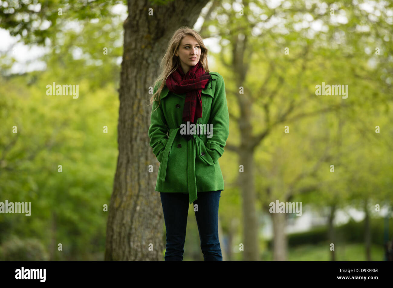 Eine junge Frau trägt einen grünen Mantel Stand selbst allein im Wald Forest Park an einem Frühlingstag, UK Stockfoto
