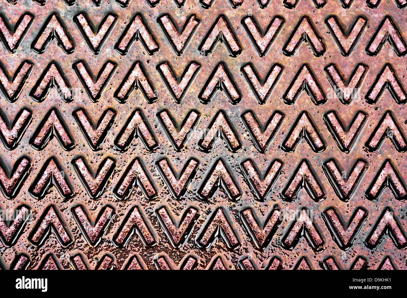 metallische Textur mit größer als und kleiner als Symbol auf einem nassen Abwasserkanal-cover Stockfoto