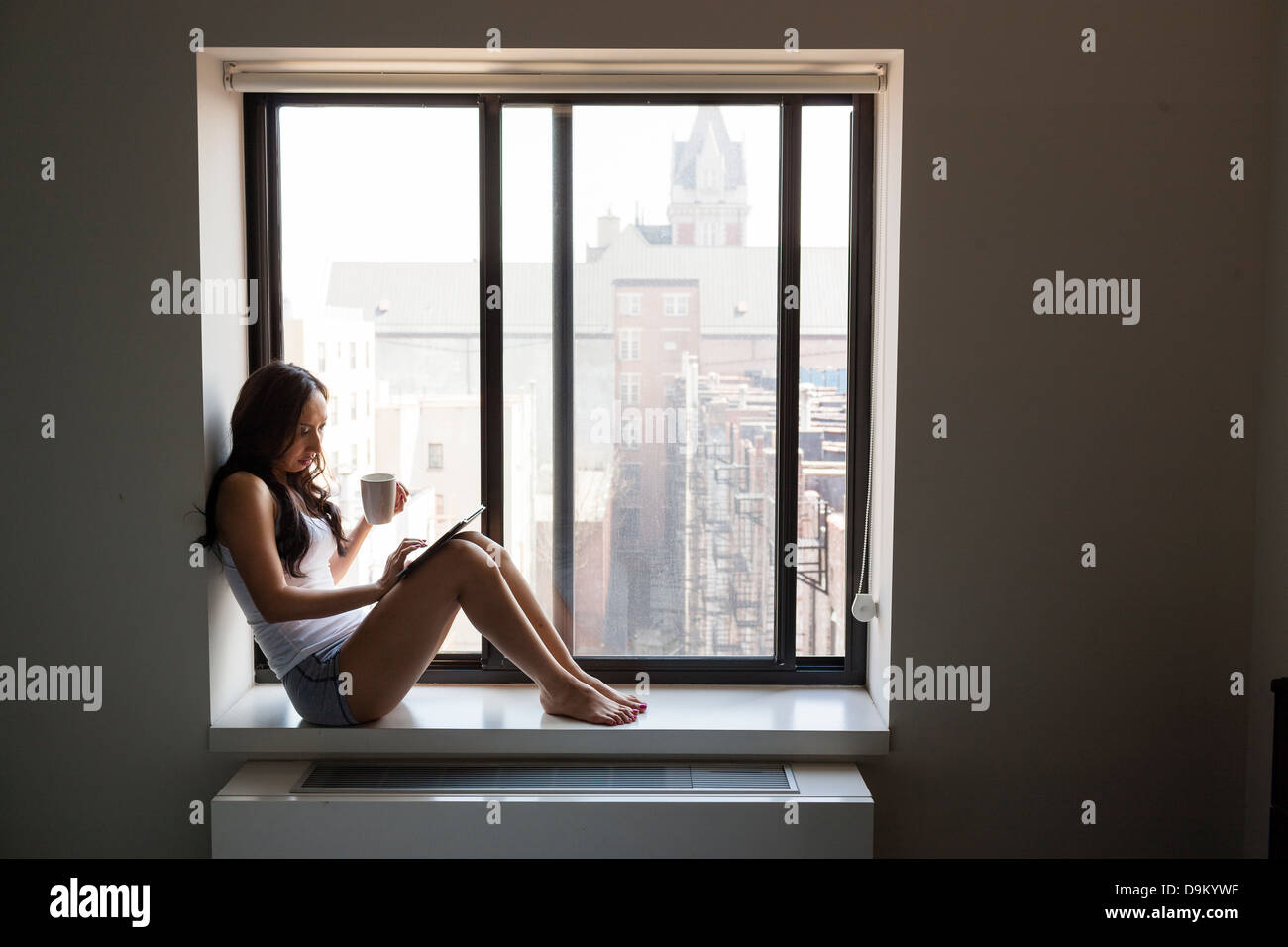 Mitte Erwachsene Frau mit Tablet auf Fensterbank Stockfoto