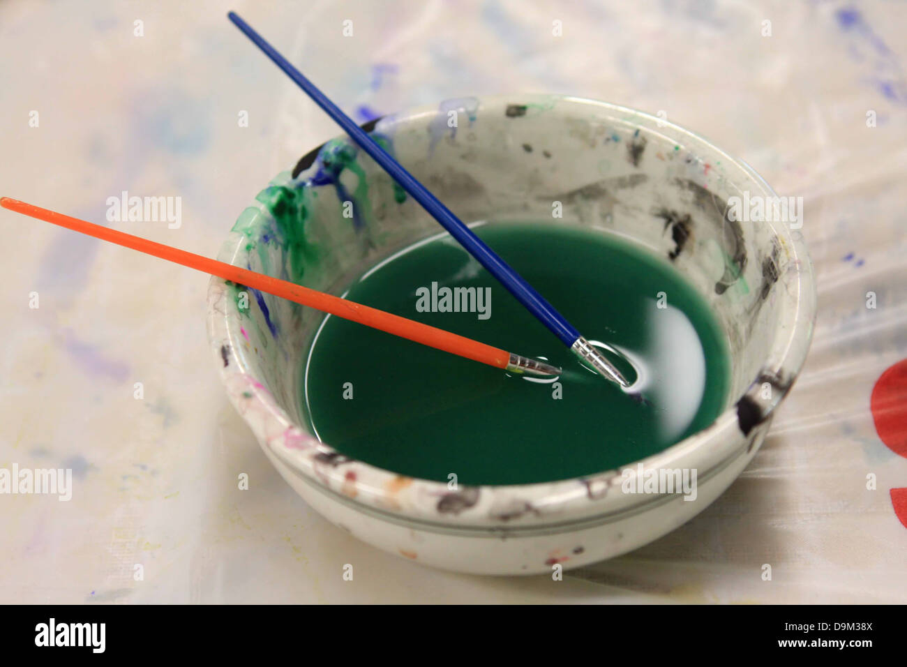 zwei Pinsel in weiße Schale mit Grün gefärbtem Wasser Stockfoto