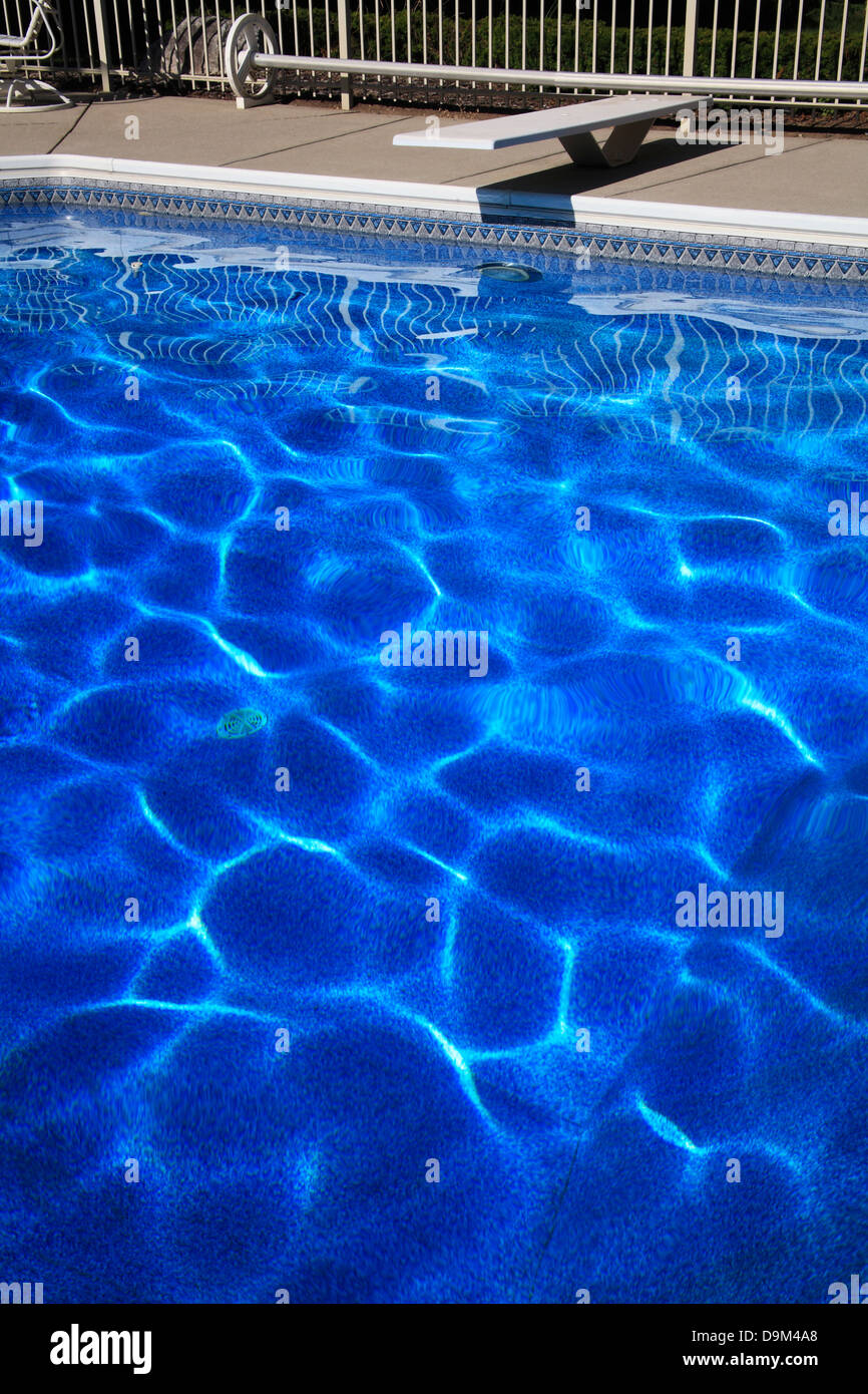 Ein Sprungbrett und tiefblaue Schwimmbadwasser bilden abstrakte Muster erstellt von Sonnenlicht auf die wellige Oberfläche tanzen Stockfoto