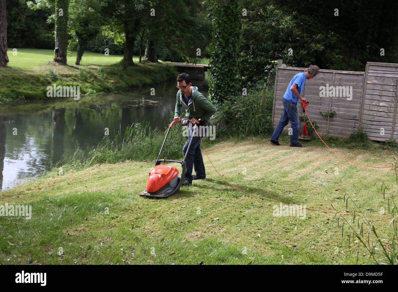 Männer arbeiten im Garten ein Mähen des Rasens mit Flymo Rasenmäher und das andere mit einem Trimmgerät Fluss Gillingham Dorset England Stockfoto