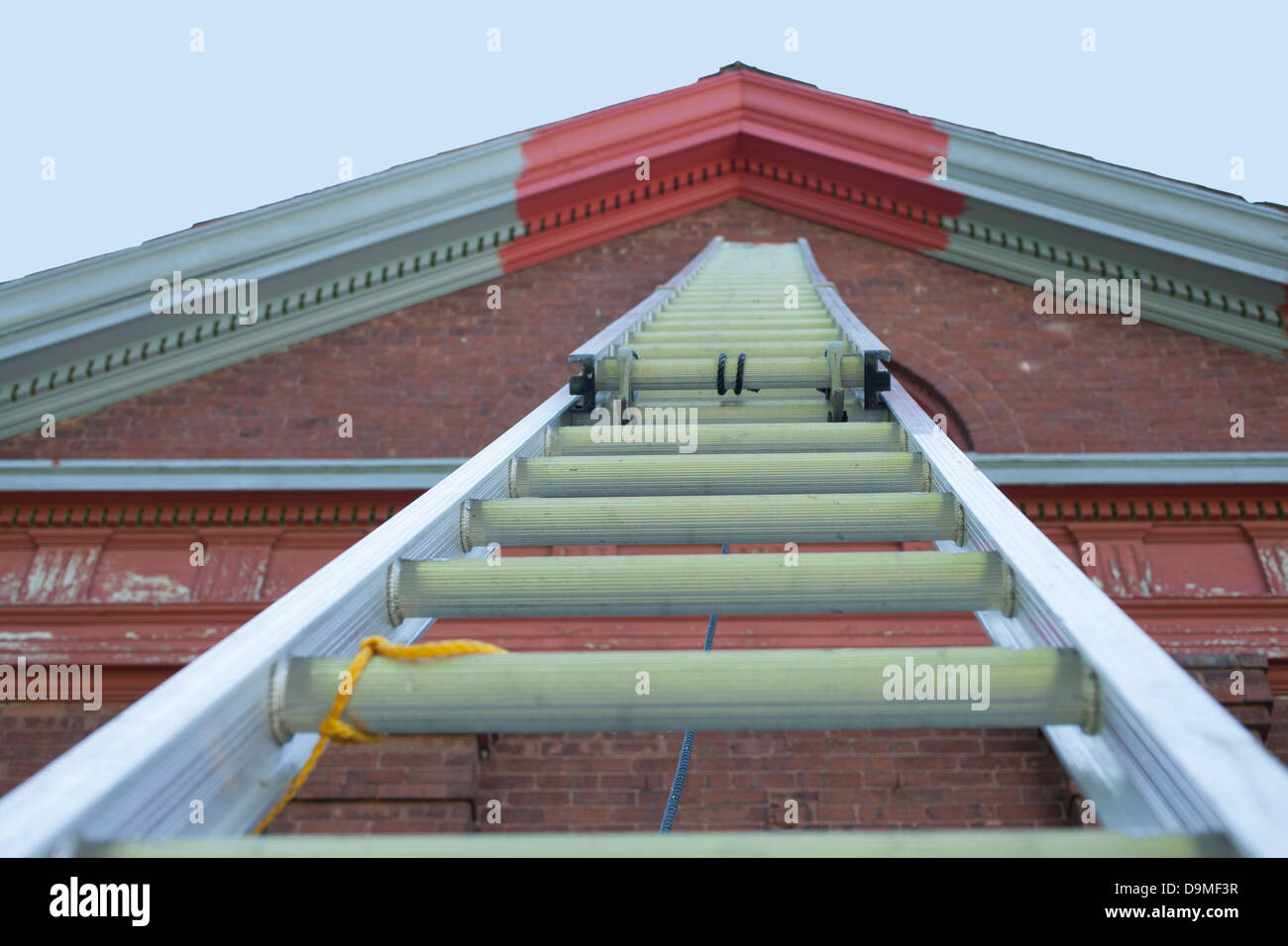 Eine sehr große Aluminium-Schiebeleiter reicht bis zur Spitze des ehemaligen Schulhaus.  Graue Farbe ist Grundierung und rot ist endgültig. Stockfoto