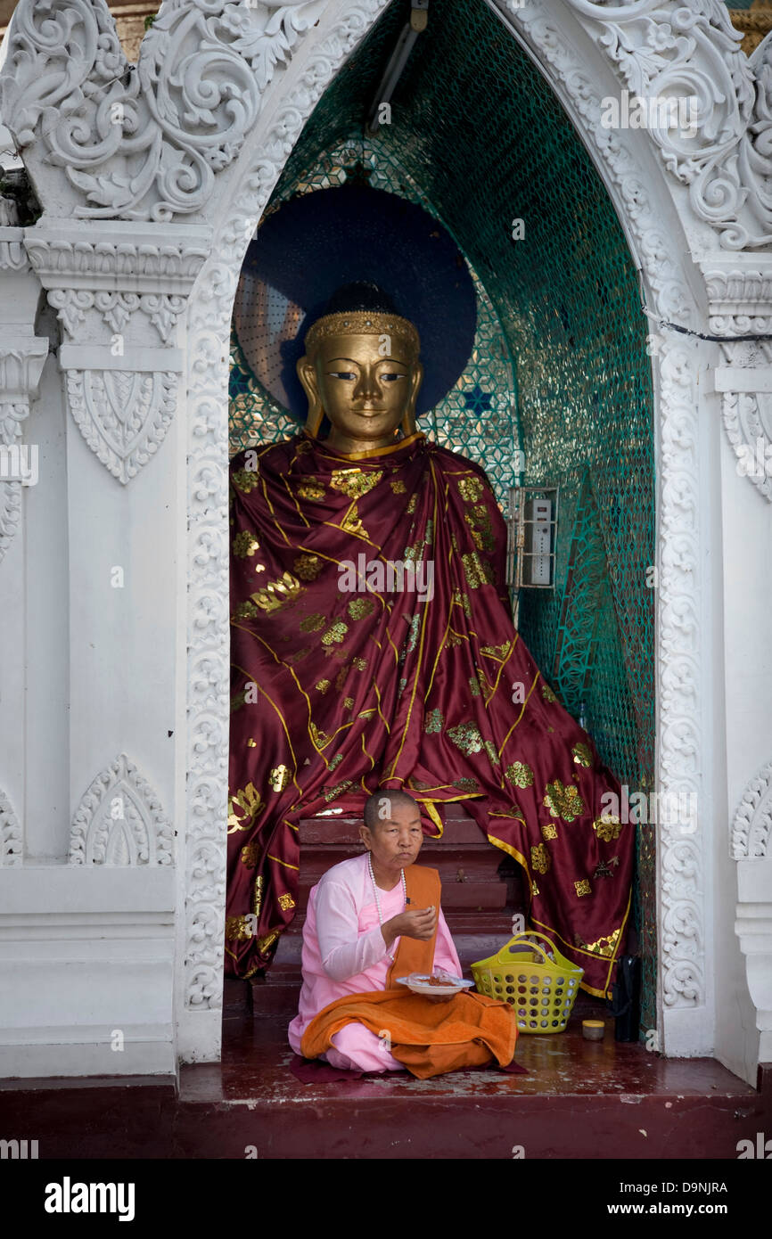 Die Shwedagon Burmas heiliger Tempel im Herzen von Rangun. Eine Nonne in ihrem rosa Gewand isst vor einem Buddha in einer Seitenkapelle. Stockfoto