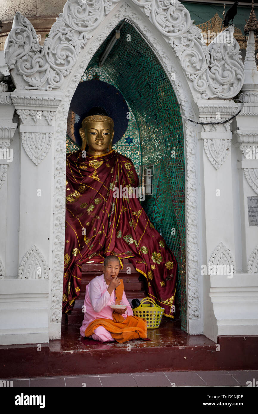 Die Shwedagon Burmas heiliger Tempel im Herzen von Rangun. Eine Nonne in ihrem rosa Gewand isst vor einem Buddha in einer Seitenkapelle. Stockfoto