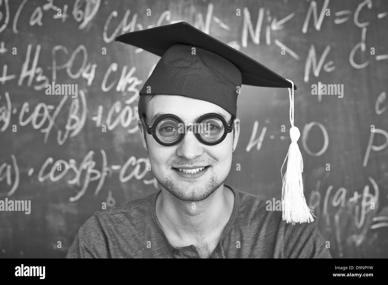 Schwarz-weiß-Bild von hübscher Student in Graduation Hut und Brille Blick in die Kamera auf Grund der Tafel Stockfoto