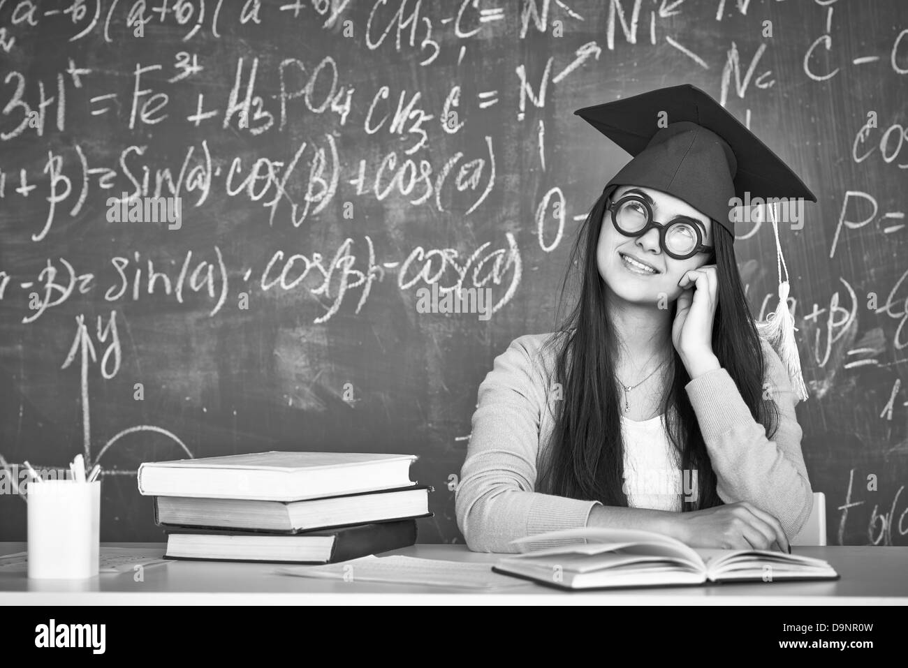 Schwarz-weiß-Bild von nachdenklichen Studenten in Graduation Hut und Brille auf Grund der Tafel Stockfoto