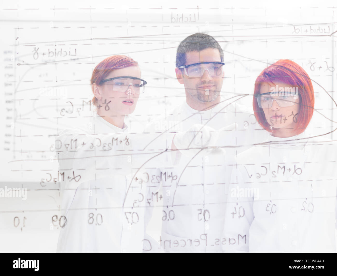Close-up durch eine transparente Board ot drei Wissenschaftler in einem Chemielabor zeigen und Analyse von Formeln darauf gesehen Stockfoto