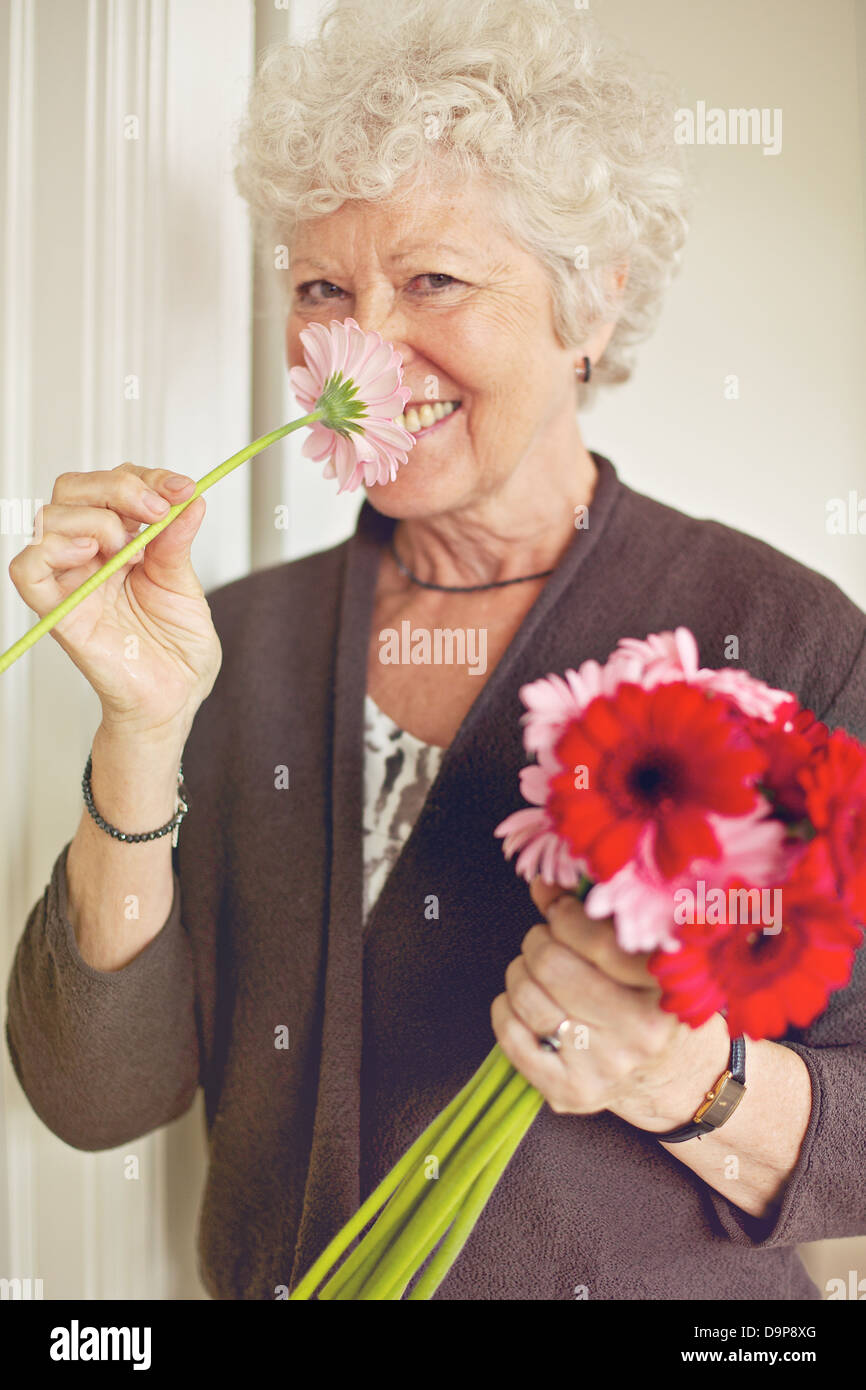 Fröhliche Senioren Dame riechen eine Blume im Innenbereich Stockfoto