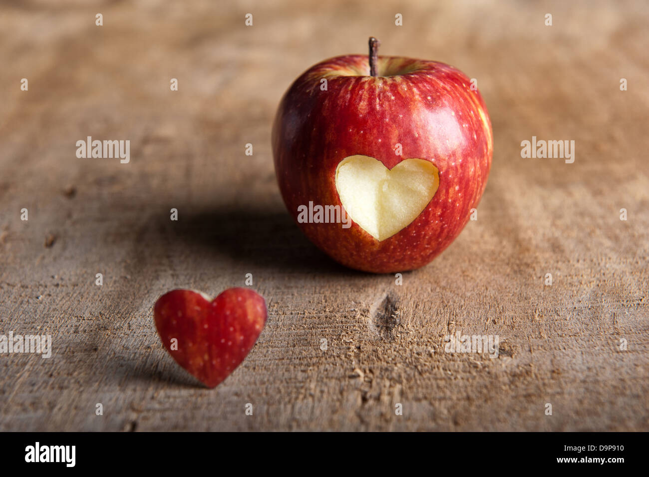 Roter Apfel mit Herz-Form ausschneiden. Die ausgeschnittenen Herzen  vor/neben der Apfel eine Warm getönten Holzoberfläche im Vordergrund. Liebe  Stockfotografie - Alamy