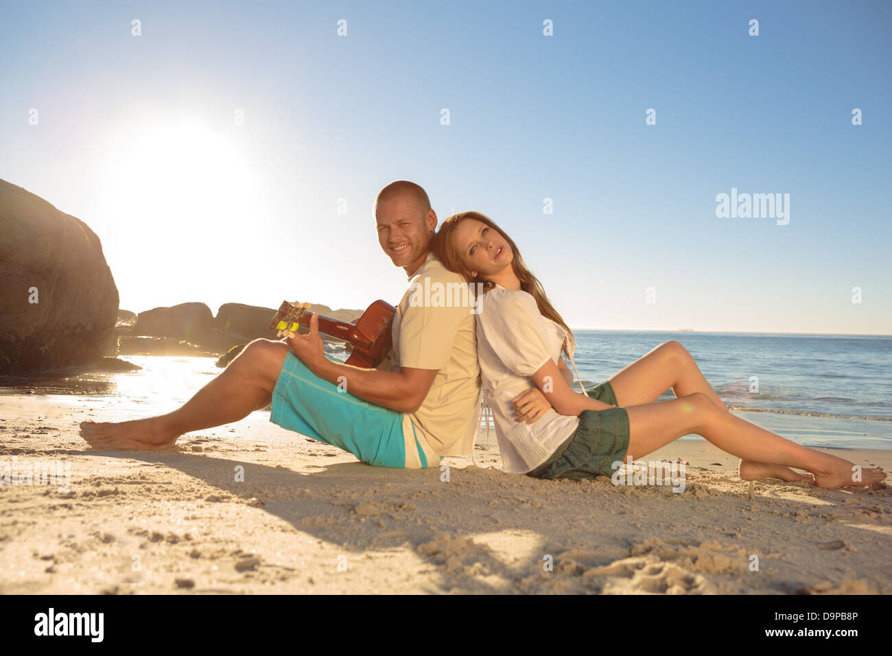 Paar saß Rücken an Rücken am Strand Stockfoto