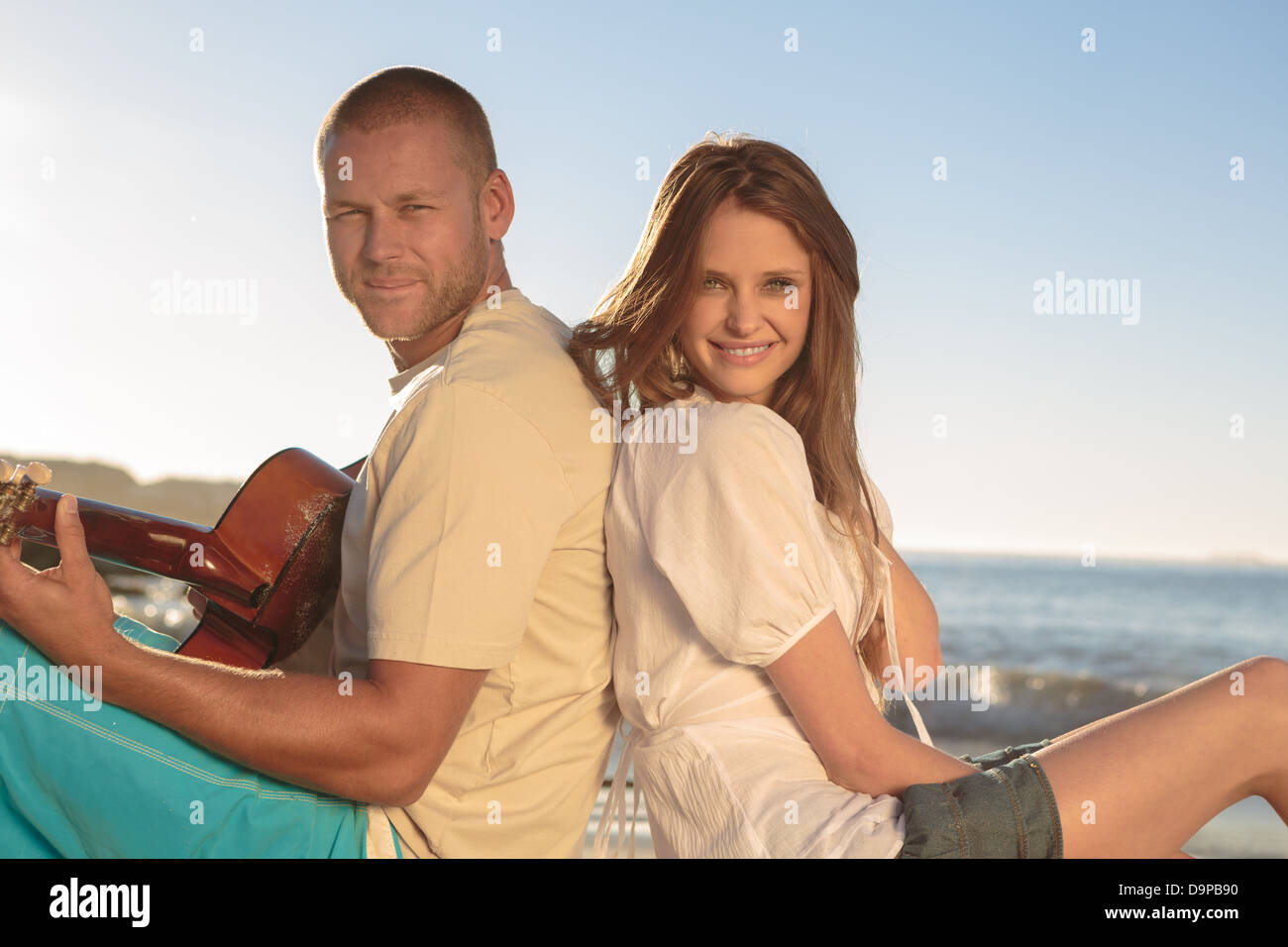 Hübsches Paar saß Rücken an Rücken am Strand Stockfoto