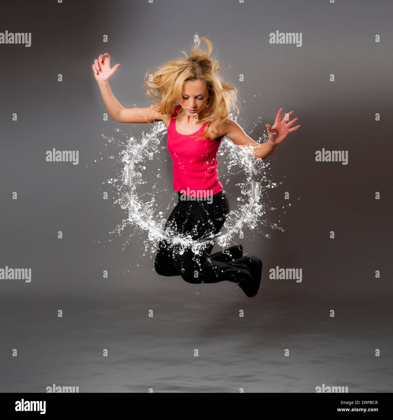 Zusammengesetzte Aufnahme einer jungen kaukasischen Frau, die durch einen kreisförmigen Wasserspritzer springt Stockfoto