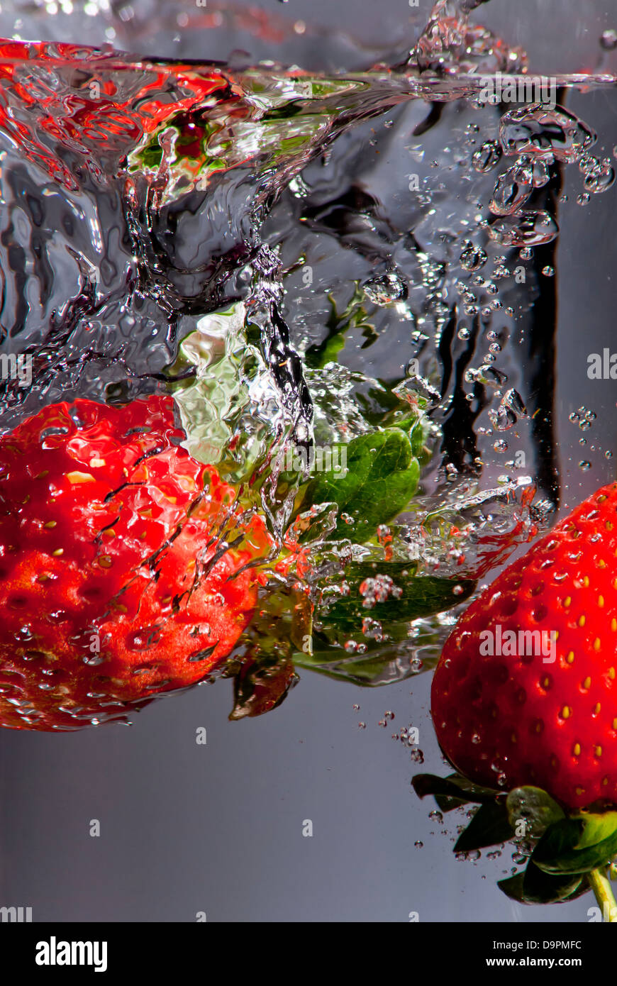 Zwei Erdbeere Spritzer ins Wasser mit einem grauen Hintergrund Stockfoto