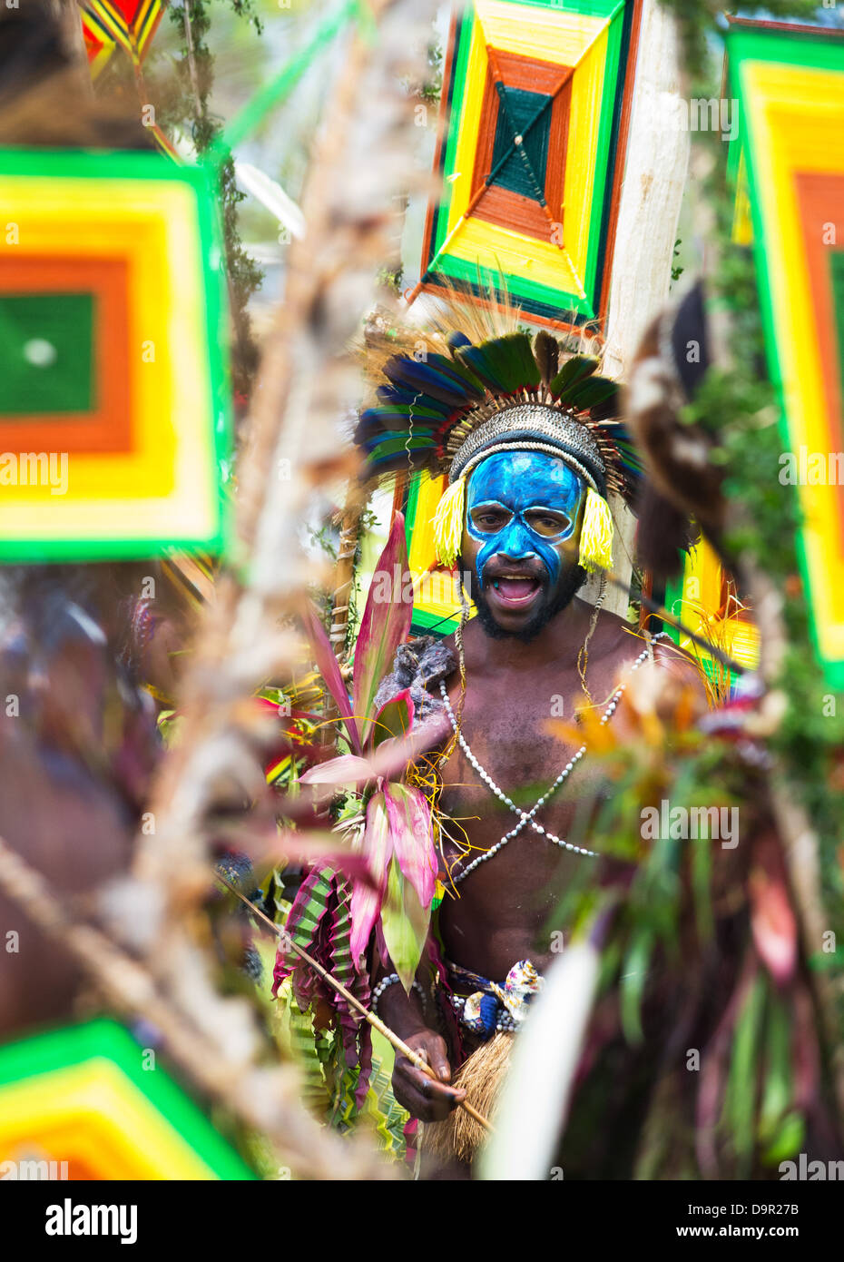 Stammes-Krieger mit seinem Gesicht gemalt mit blauer Farbe, umgeben von Stammes-Fahnen und schreien, Goroka Show, Papua New Guinea Stockfoto