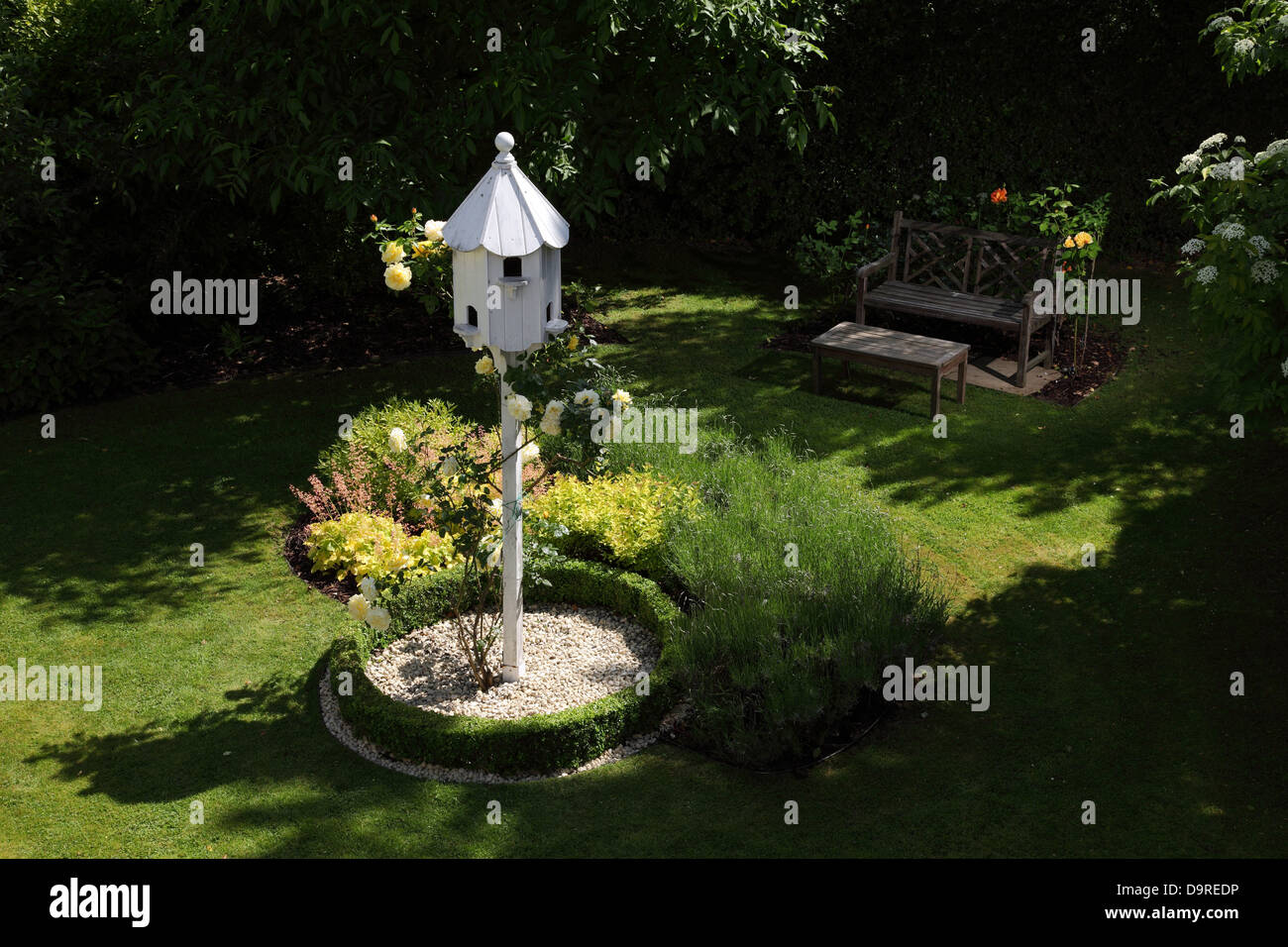 Ein weißer Taubenschlag, umgeben von niedrigen Kasten Absicherung und weißen Steinen mit einem gelben Rosenzucht bis es in einem Garten Stockfoto