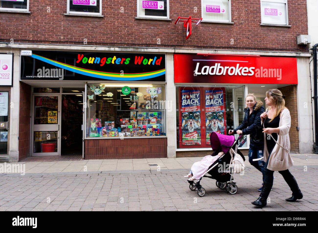Menschen (Bewegung verwischt) vorbei an Zweigen von Ladbrokes und Jugendlichen Welt-Spielzeug-Shop. Stockfoto