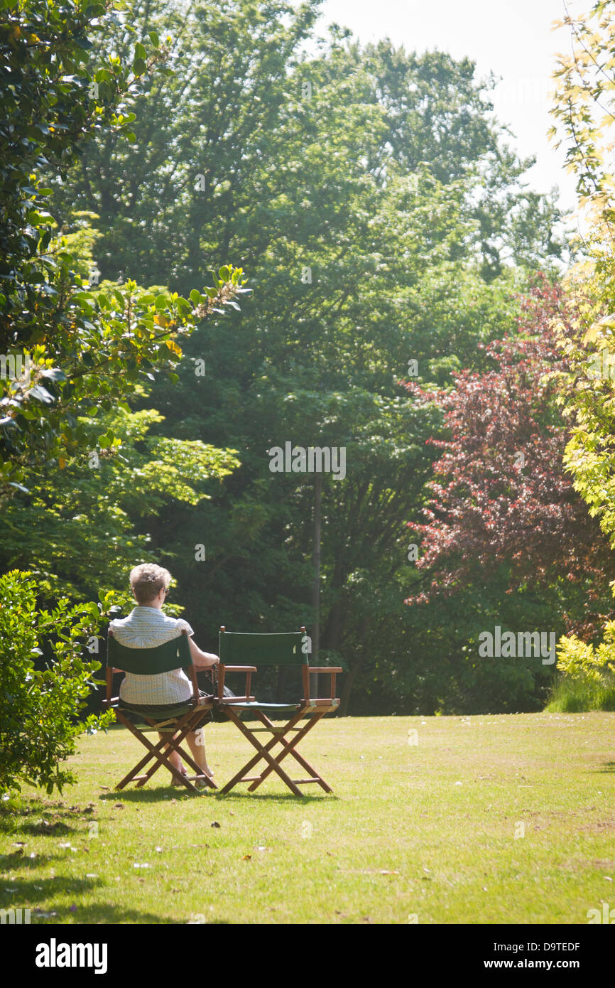 Eine Frau sitzt allein las das Papier in einem englischen Park im Sommer Stockfoto