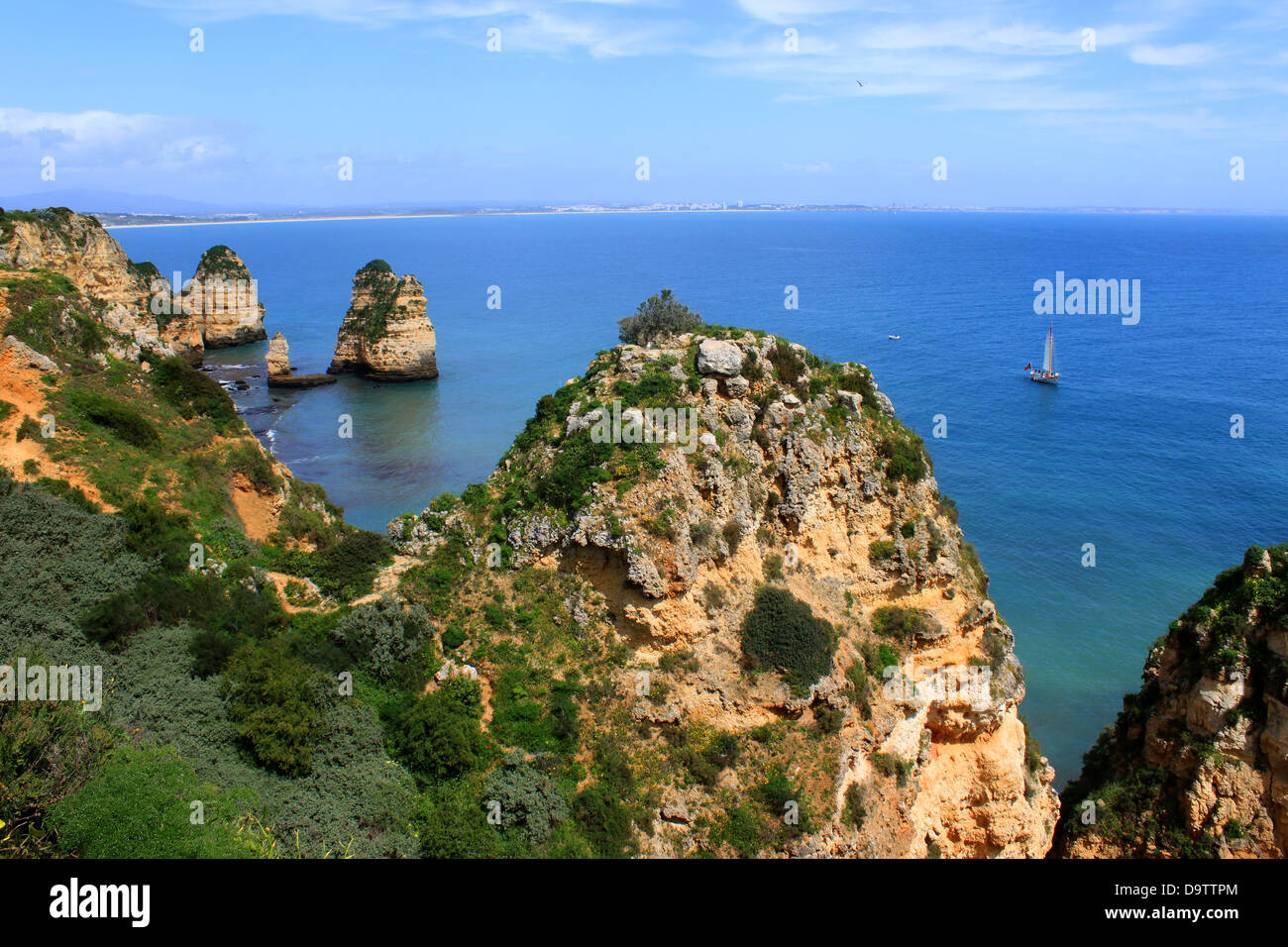 Felsen an der Küste des Atlantischen Ozeans in Lagos, Algarve, Portugal mit Segelboot in der Ferne Stockfoto