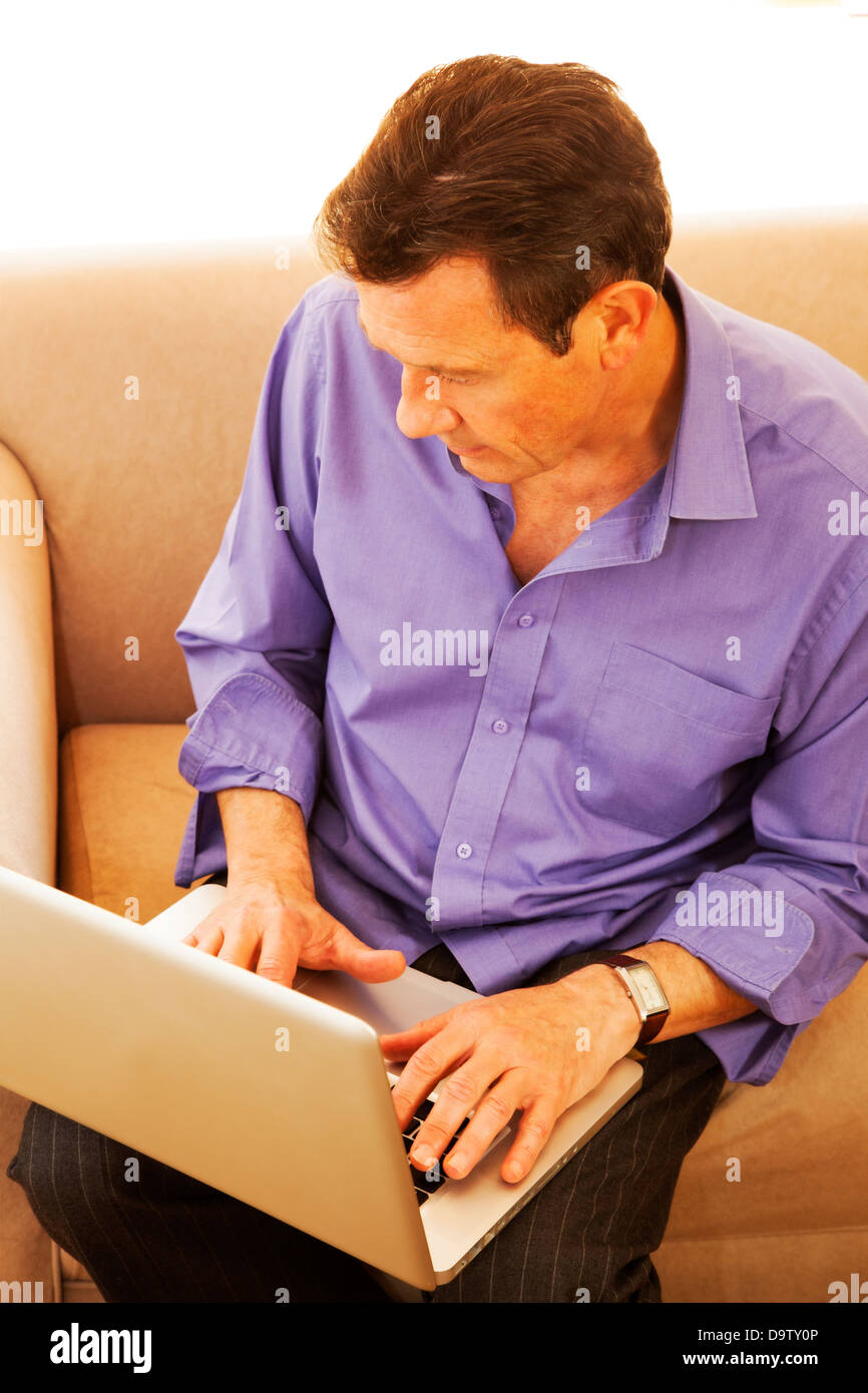 Blick hinunter auf ein Mann sitzt auf einem Sofa mit einem Laptop. Stockfoto