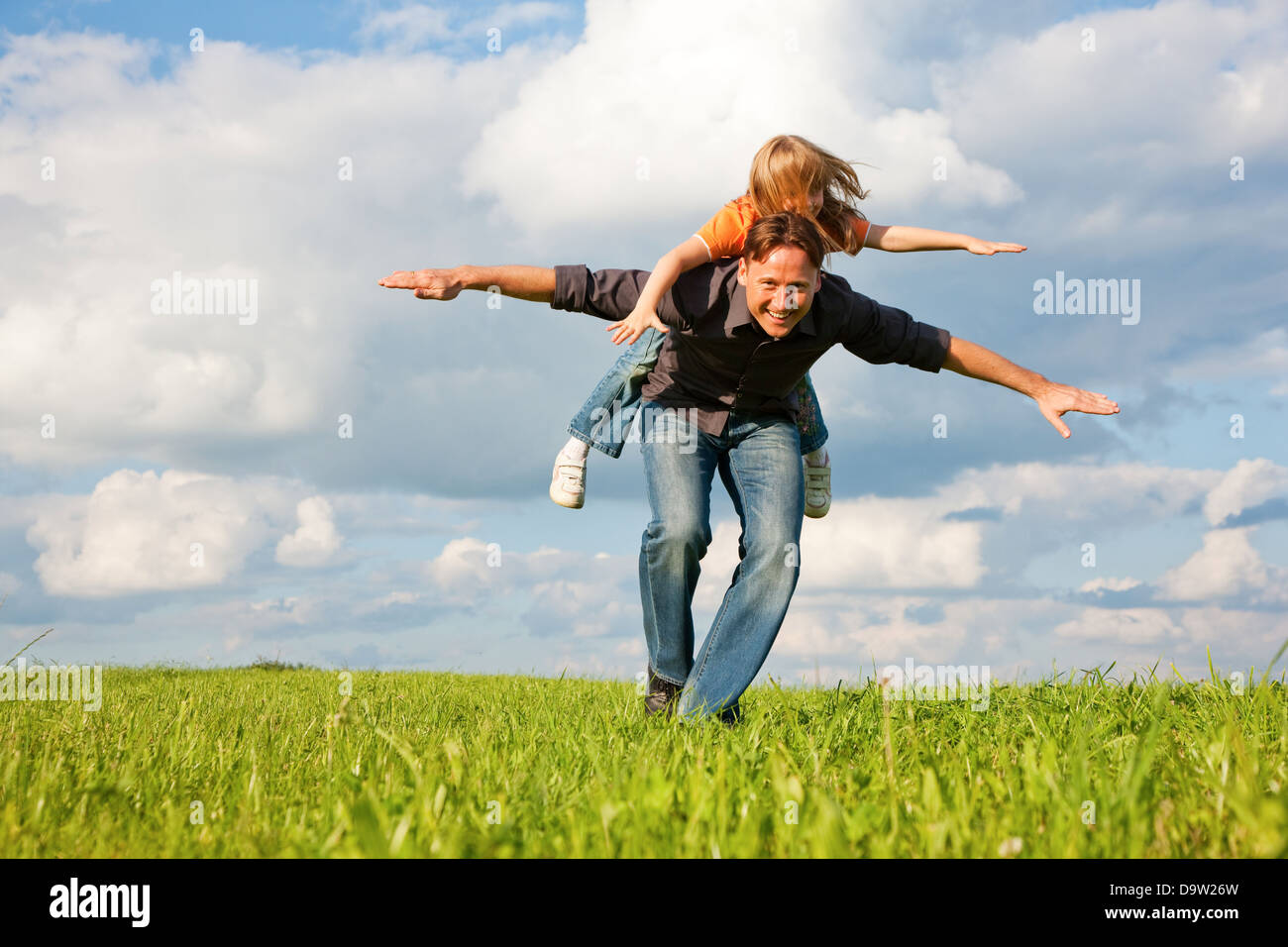 Vater und sein Kind - Tochter - zusammen auf einer Wiese zu spielen, ist er ihr Huckepack tragen. Stockfoto
