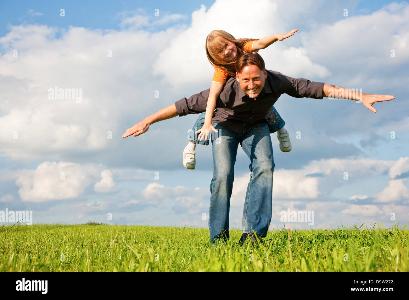 Vater und sein Kind - Tochter - zusammen auf einer Wiese zu spielen, ist er ihr Huckepack tragen. Stockfoto